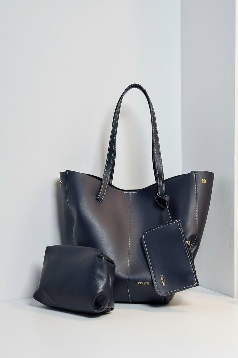 Set of black leather handbags including a tote, small bag, and wallet on a light gray background